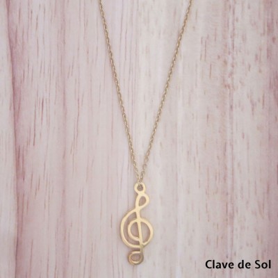 Colar dourado com pendente clave de sol, fundo madeira clara