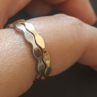 Anel de duas bandas metálicas onduladas prateada e dourada num dedo
