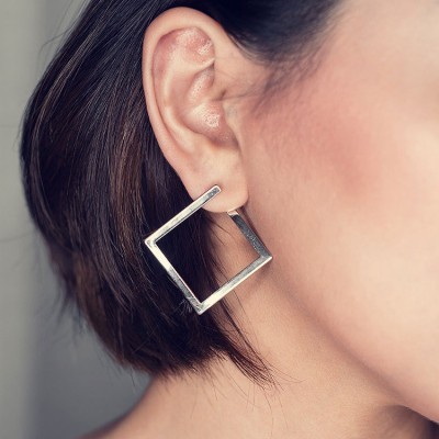 Brinco quadrado em metal prateado na orelha de mulher com cabelo castanho curto