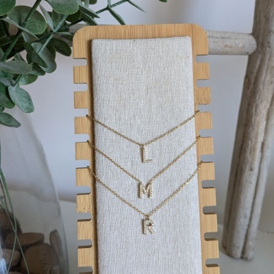 Expositor de colares com letras L, M e R em fundo de tecido cru e estrutura de madeira