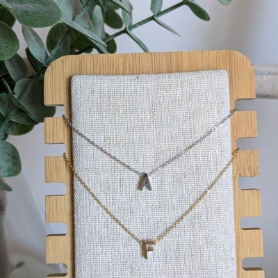 Dois colares com letras em base de madeira e tecido com folhas ao fundo