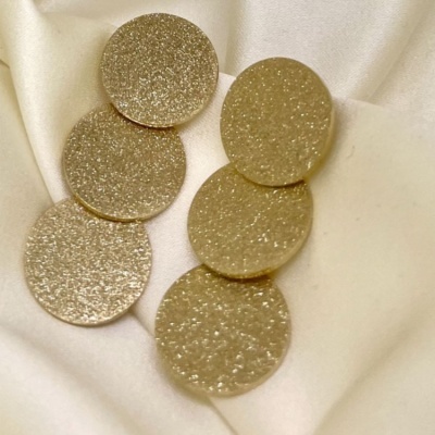 Brincos redondos dourados com textura rugosa sobre tecido branco