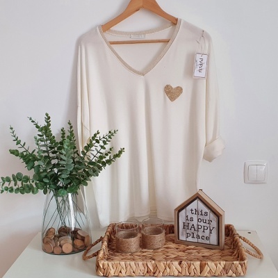 Camisola bege clara com coração dourado, vaso com plantas e bandeja com velas e placa decorativa