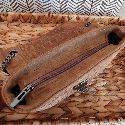 Bolsa bege com padrão de pele de crocodilo e alça de corrente prateada sobre superfície de palha