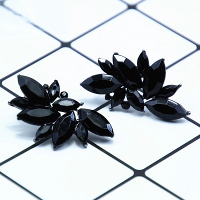 Brincos pretos em forma de folhas sobre superfície branca com padrão geométrico