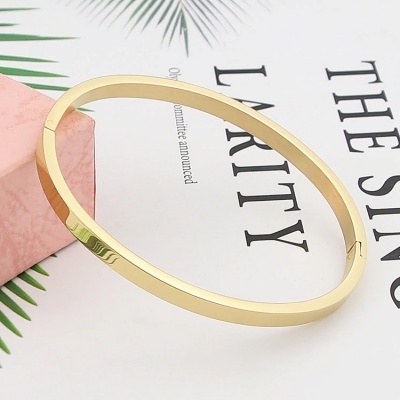 Pulseira de metal dourado com fecho seguro sobre superfície branca com texto e caixa cor-de-rosa