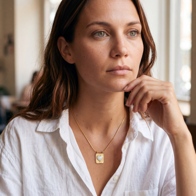 Colar dourado com pendente de coração e mulher de camisa branca