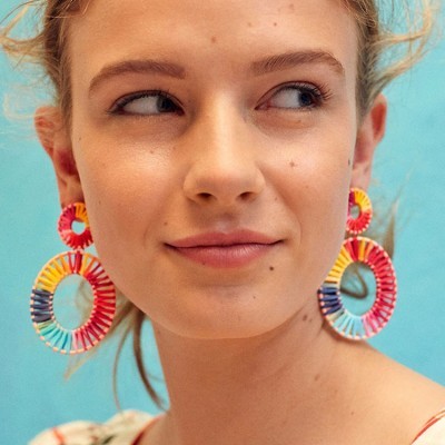 Brincos grandes coloridos redondos em mulher com fundo azul