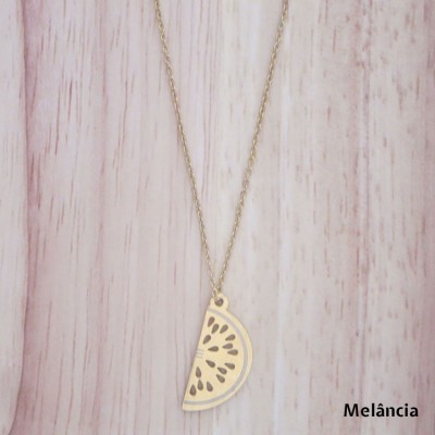 Colar dourado com pendente em forma de meia-lua de melancia sobre fundo de madeira clara