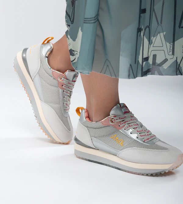 Sapatilhas Anekke Smart Sapatilhas cinzentas e rosa com sola branca usadas por pessoa com vestido azul claro com letras