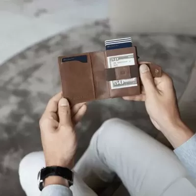 Carteira em couro castanho com cartões, mão de homem segurando, sentado em sofá cinzento