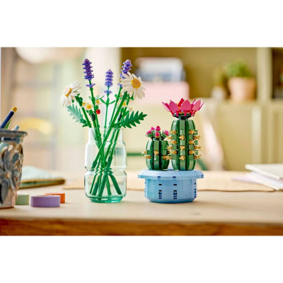 Flores artificiais em vaso de vidro e vasos plásticos com plantas artificiais sobre mesa de madeira