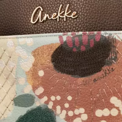 Carteira estampada Anekke com logo metálico em fundo castanho e padrões coloridos