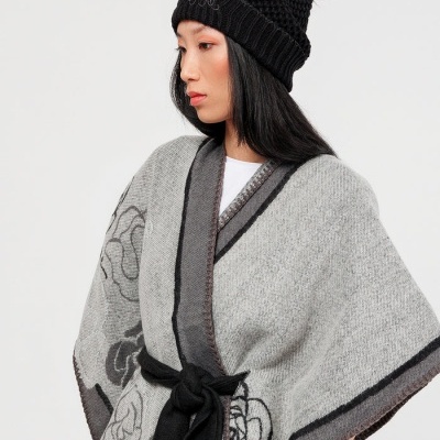 Mulher com camisola de malha cinzenta com padrão floral e gorro preto com pompom