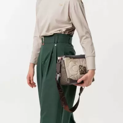 Mala de mão bege e castanha com padrão e alça decorada, segurada por mulher com roupa bege e verde