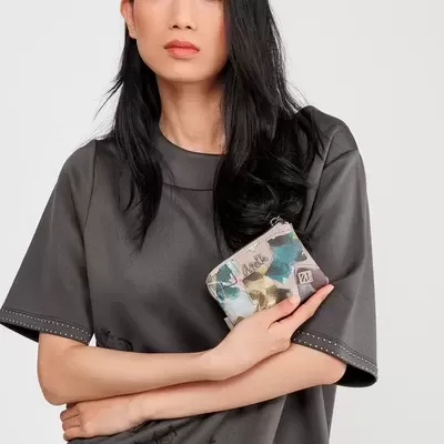 Mulher com camisola cinzenta segurando carteira pequena com padrão colorido