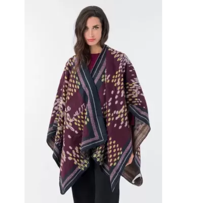 Mulher a usar poncho vinho com padrão de bolinhas amarelas e lilás e bordas com riscas azuis e rosas.
