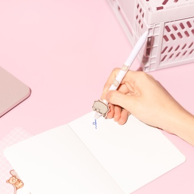 Caneta decorada com gatos a desenhar num caderno branco num ambiente cor-de-rosa