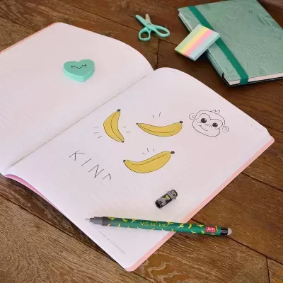 Caderno aberto com desenhos de bananas e macaco, caneta, borracha de coração e acessórios de papelaria