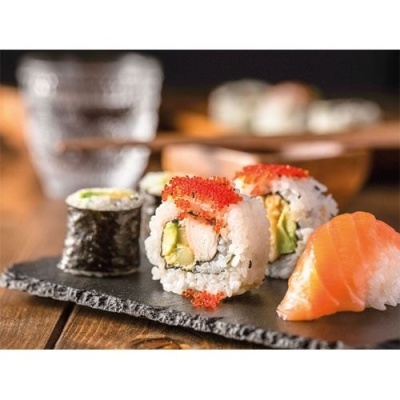 Prato de sushi variado com nigiri de salmão e sushi enrolado em pedra negra sobre mesa de madeira