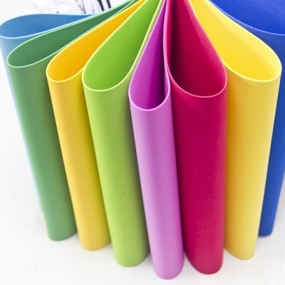 Folhas plásticas coloridas organizadas em ondas sobre superfície clara.