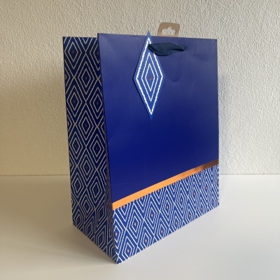 Saco de papel azul com padrão geométrico branco e azul, alça azul e detalhe laranja.
