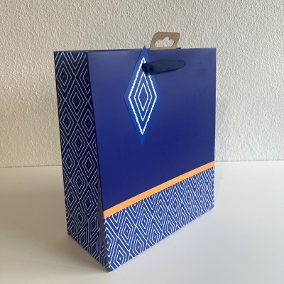 Saco de papel azul decorativo com padrões geométricos e pega de fita