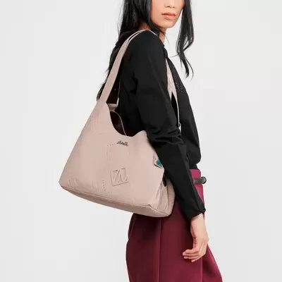 Modelo com mala de ombro bege, camisola preta e calças bordô, fundo branco