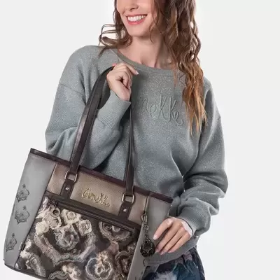 Mala de mão feminina com padrão abstrato em tons castanho e cinzento segurada por mulher com camisola cinzenta.