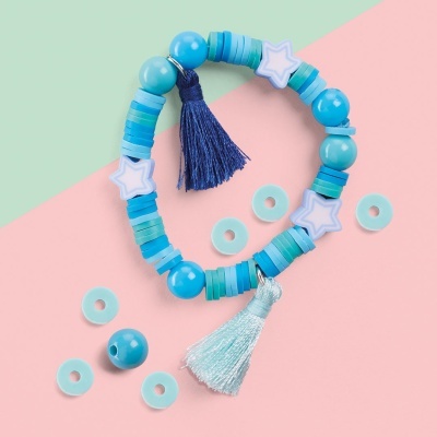 Pulseira elástica azul com pompons e contas redondas sobre fundo verde claro e rosa.