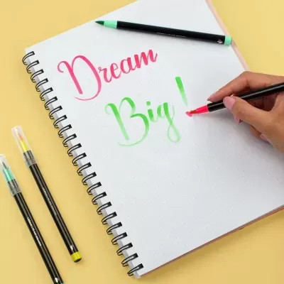 Caderno espiral branco com texto colorido e marcadores de ponta pincel sobre fundo amarelo