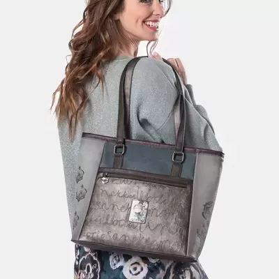 Mulher com blusão cinzento e saia floral a segurar uma mala de senhora castanha e cinzenta com padrão de escrita