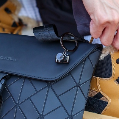 Bolsa preta com padrão geométrico, chaveiro de câmara e bota castanha com forro de pelo