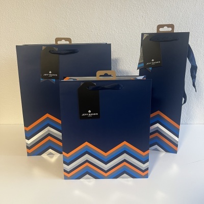 Sacos de papel azul escuro com padrão em chevron colorido e etiquetas pretas JEFF BANKS