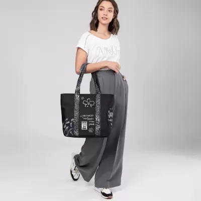 Mulher com mala preta estampada, t-shirt branca e calças cinzentas largas em fundo cinzento claro