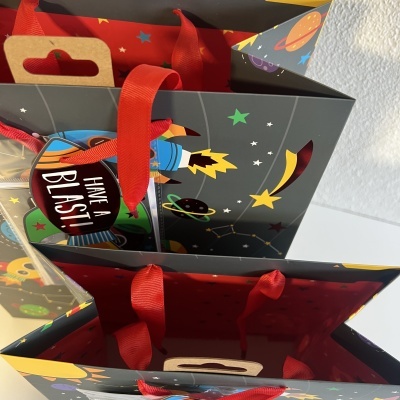Sacos de presente com tema espacial e etiqueta 'HAVE A BLAST!' com alças vermelhas