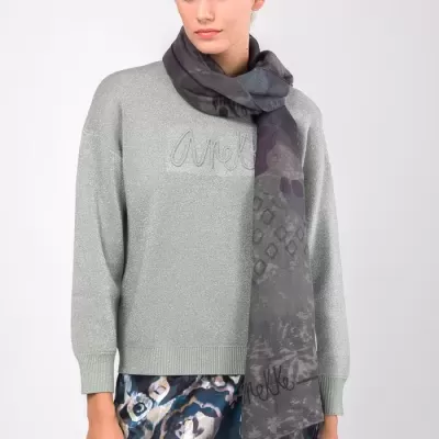 Mulher com camisola cinza, cachecol cinza escuro e saia estampada azul e branco