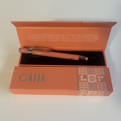 Caneta cor de terracota com detalhes prateados numa caixa decorativa da mesma cor.