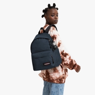 Pessoa a usar mochila azul escura Eastpak com garrafa de água e roupas tie-dye e calças azuis.