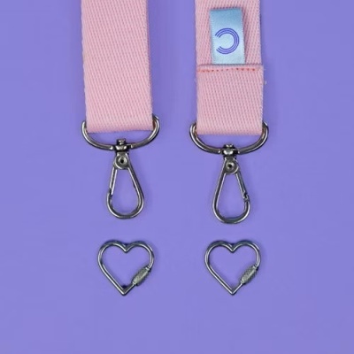 Fitas rosa com mosquetões prateados e mosquetões em forma de coração sobre fundo lilás