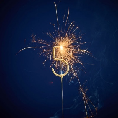 Vela dourada em forma do número 5 a arder com faíscas brilhantes.