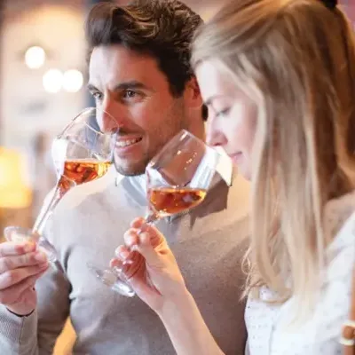 Homem e mulher segurando copos de vinho rosé em ambiente interno