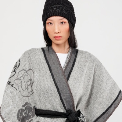 Mulher com poncho cinzento com padrão de rosas e gorro preto com pompom