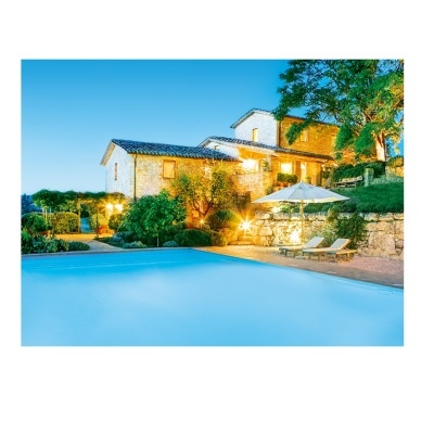 Piscina com espreguiçadeiras e guarda-sol junto a casa de campo iluminada ao entardecer