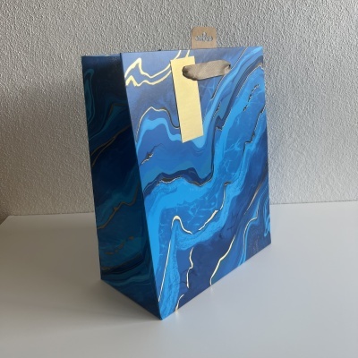 Saco de presente azul marmoreado com alças bege e etiqueta amarela
