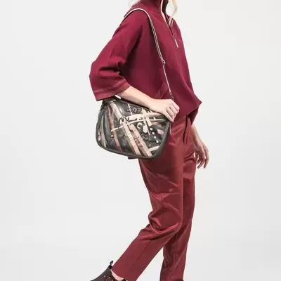 Mulher com roupa cor de vinho, botas e mala de ombro com padrão escrito