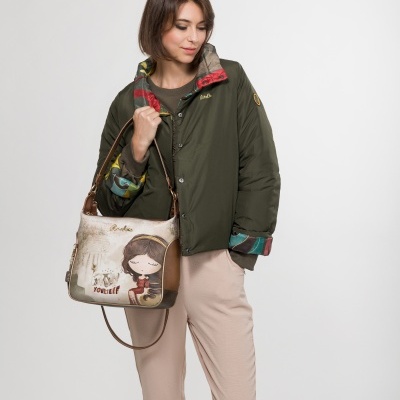 Mulher com jaqueta verde escura, calças bege claras e mala de ombro bege com desenho e texto