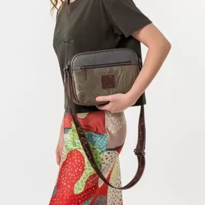 Bolsa pequena castanha e preta com alça ajustável segurada por mulher com roupa colorida