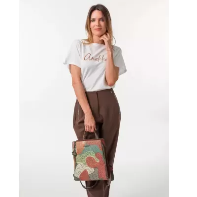Mulher com camisola branca e calças castanhas segurando mala de mão colorida