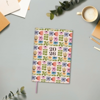 Agenda 2026 com capa floral colorida e marcador rosa sobre mesa cinza